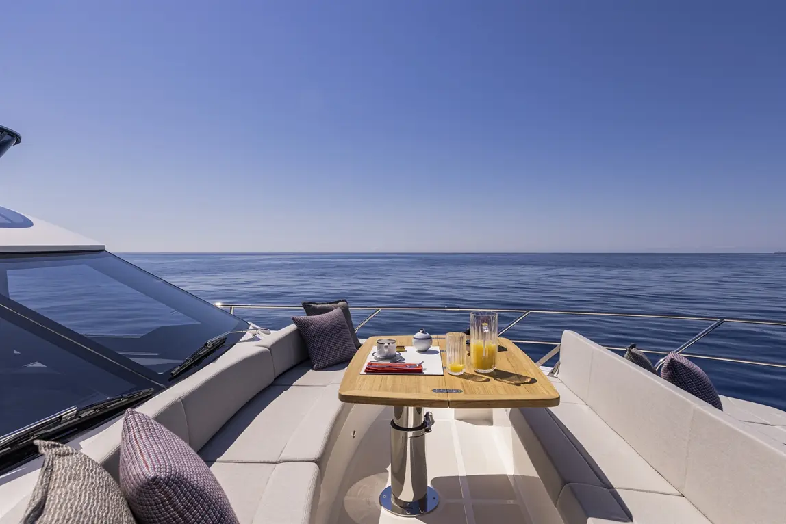 Luxurious yacht deck with a wooden table set for breakfast, featuring drinks and snacks, overlooking calm blue waters and clear sky.